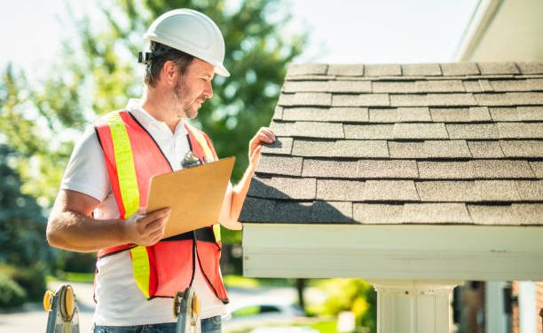 A man with hard hat standing on steps inspecting house roof