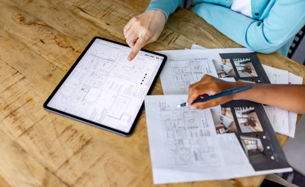 Close-up on a woman looking at the blueprints of a house for sale with her real estate agent using a digital tablet